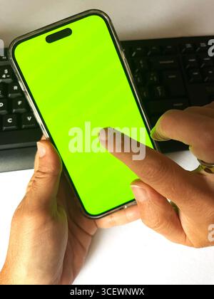 Vertical view of woman's hands holding her phone with a green screen Ideal for on line working ads. Stock Photo