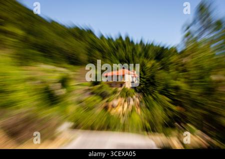 Zoom blur applied to a stone house with a red roof in a green forest, creating abstract motion effect. Stock Photo