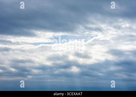 Cloudy Sky with Sunlight Breaking Through Layers – Blue Sky Peeking from Behind Storm Clouds. Stock Photo