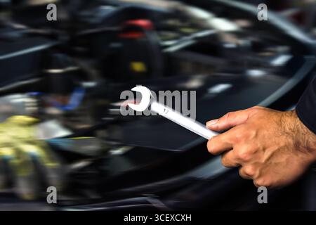 Car repair close up, mechanic hand holding open-end wrench in engine bay, blurred workshop background Stock Photo