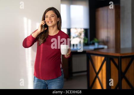 A joyful adult pregnant woman laughing and talking on her mobile phone while relaxing at home Stock Photo