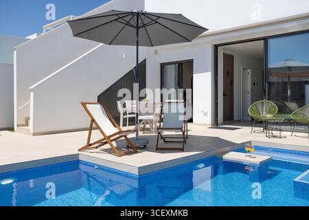 Contemporary villa with pool, lounge chairs, umbrellas and stairs leading to a private rooftop terrace. Stock Photo