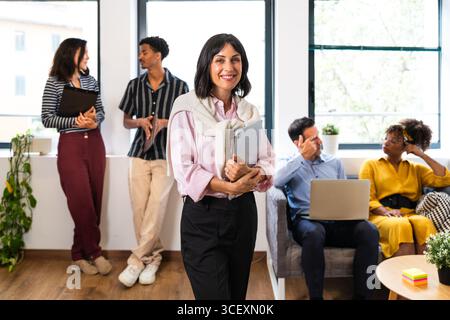 Businesswoman holding tablet smiling leading diverse team discussing and working in modern office, collaborating on project in startup environment, sh Stock Photo