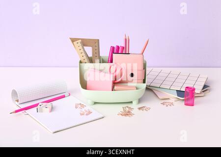 Holder with different stationery and notebooks on light desk Stock Photo
