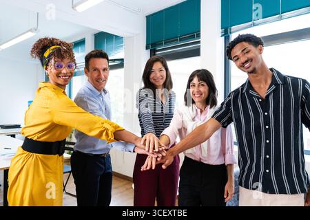 Five smiling colleagues joining hands in a modern office, celebrating teamwork and unity while demonstrating commitment to collaboration and project s Stock Photo
