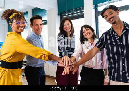 Five smiling business people joining hands in the office, demonstrating teamwork and collaboration in a startup environment, promoting unity and share Stock Photo