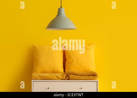 Pillows with folded blankets on commode near yellow wall in room Stock Photo