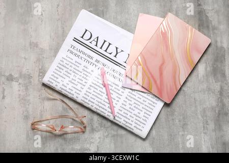Daily newspaper with glasses and notebooks on grey grunge background Stock Photo