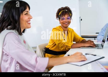 Two businesswomen are collaborating on a project, using a laptop and taking notes during a productive office meeting, showcasing teamwork and technolo Stock Photo