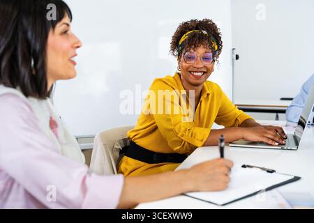 Two businesswomen collaborating on a laptop during a dynamic office meeting, exchanging innovative ideas and strategies to drive success and achieve t Stock Photo