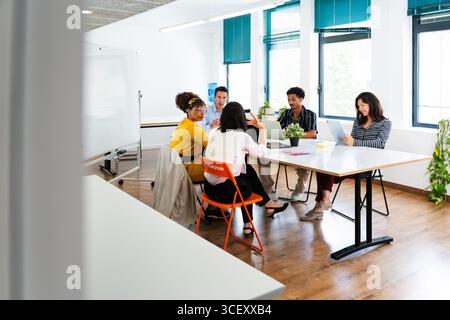 Diverse team of professionals are having a productive meeting in a contemporary office space, engaging in teamwork and utilizing technology for a coll Stock Photo