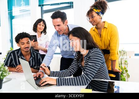 Business team collaborating on a project, using a laptop, in a modern startup office, working together to achieve a common goal, sharing ideas and exp Stock Photo