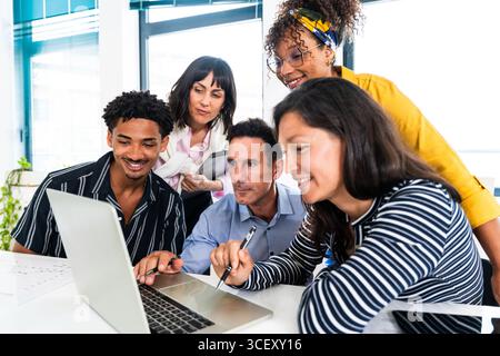 Diverse team of professionals gathered around a laptop, actively discussing and collaborating on a project during a productive meeting in a modern sta Stock Photo