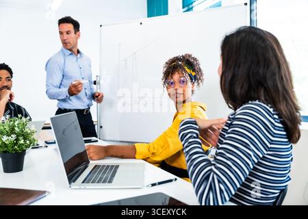 Business colleagues are collaborating on a project, analyzing data on a whiteboard and laptop, and engaging in productive discussions during an office Stock Photo