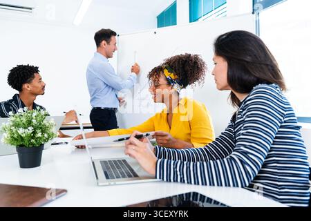 Diverse colleagues are collaborating on a project, with a manager presenting growth charts on a whiteboard during a productive office meeting, fosteri Stock Photo