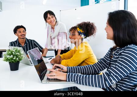 Diverse colleagues are collaborating on project, using laptops and sharing ideas in bright, modern office environment, fostering teamwork and innovati Stock Photo