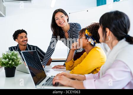 Startup business team collaborating on a project during an office meeting, engaging with laptops and exchanging innovative ideas in a bright, modern w Stock Photo