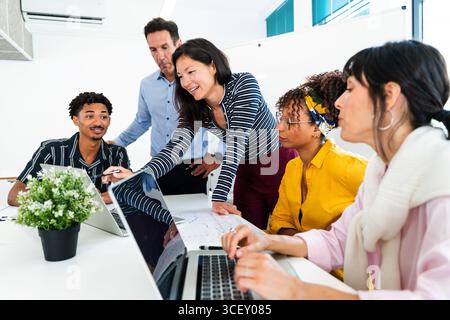 Diverse team of professionals working together, analyzing data on laptops and discussing strategies during a productive meeting in a modern startup of Stock Photo