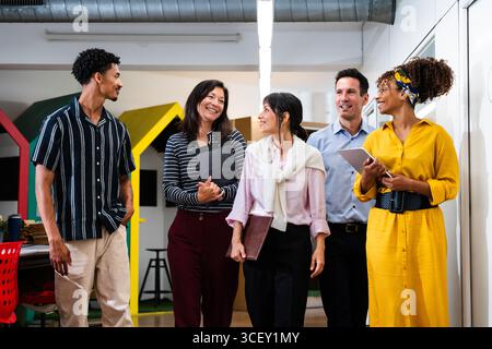 Multi-ethnic business team walking and talking together in modern office, discussing project details and sharing ideas during productive workday Stock Photo