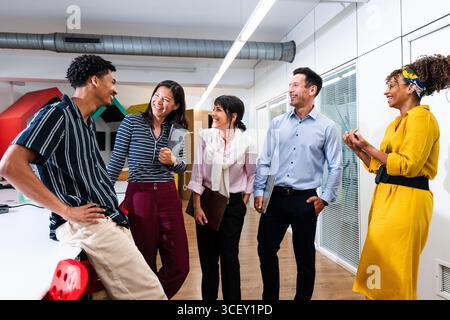 Five cheerful multiethnic colleagues are discussing and sharing new ideas, enjoying a positive and collaborative work environment in a modern office s Stock Photo