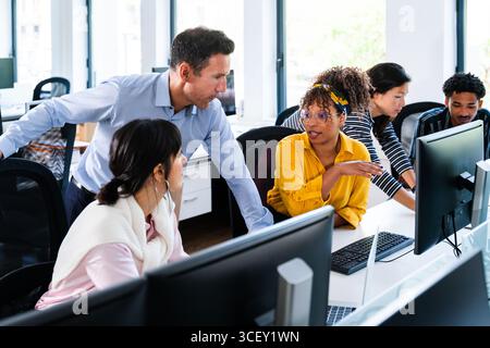 Diverse team of business professionals collaborating and working together on computer projects in a modern office startup environment, discussing stra Stock Photo