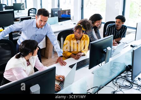 Diverse group of business professionals are working together in a modern office, using desktop computers and laptops, collaborating on a project under Stock Photo