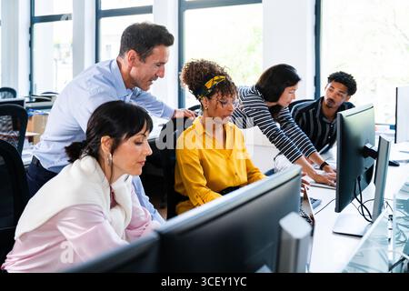 Diverse team of business professionals working together on computers, collaborating and problem-solving in a bright, modern office environment, showca Stock Photo