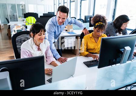 Office workers are collaborating on a project, using computers and laptops, with a manager overseeing their work in a modern office environment, highl Stock Photo