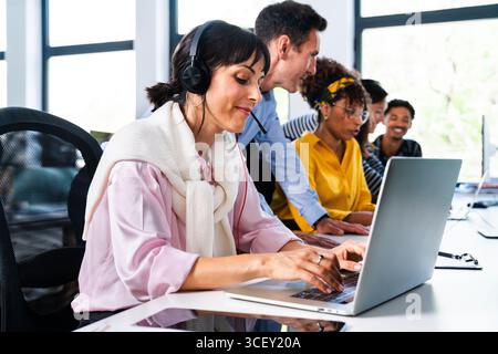 Business team collaborating and problem-solving together in a modern office environment, focusing on a customer service representative using a laptop Stock Photo