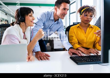 Business colleagues are working together, analyzing data on a computer screen during an office meeting, demonstrating teamwork and collaboration Stock Photo