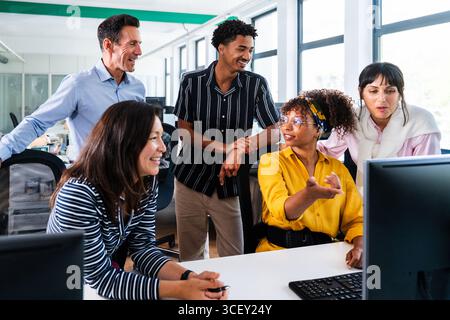 Diverse team of professionals gathered around computer, engaging in productive discussion and teamwork, fostering collaborative spirit in modern offic Stock Photo