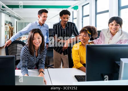 Diverse team of professionals working together in a modern office, collaborating on a project using desktop computers and laptops, showcasing teamwork Stock Photo