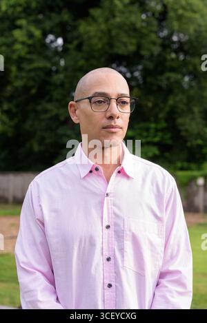 Bald Hispanic mature male in 40s wearing pink shirt and eyeglasses outdoors with camping park environment and caravan background. Concept of travel, t Stock Photo