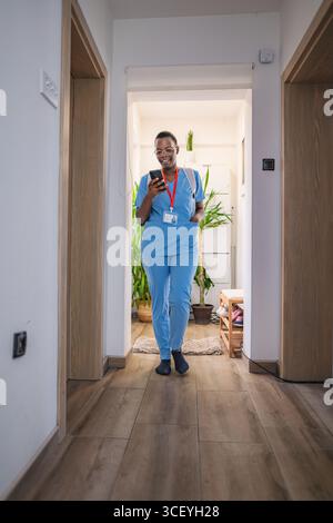 Young female doctor in blue scrubs using her smartphone at home Stock Photo