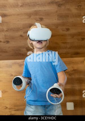 Child experiencing virtual reality using headset and controllers, engaging with immersive technology for gaming and entertainment Stock Photo