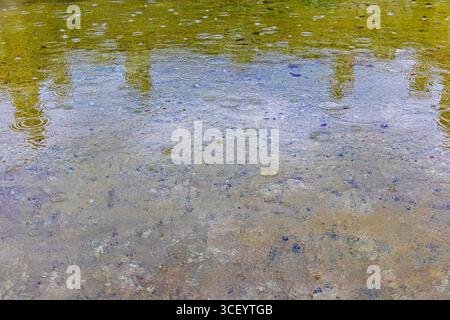 Raindrops creating ripples in shallow fountain water. Close-up of rain falling on a shallow fountain surface, forming circular ripples and subtle Stock Photo