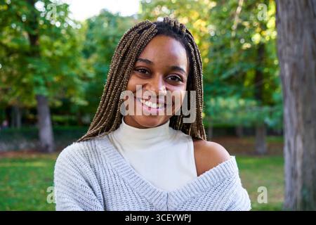 Happy young black woman, standing outdoors in a public park looking at camera smiling. Stock Photo