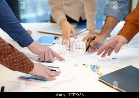 A group of professionals analyzing charts and discussing strategies during a collaborative office meeting. Documents, charts, and hands are visible, emphasizing teamwork and communication. Stock Photo