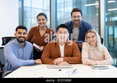 A diverse team of five professionals collaborating in a sleek, modern office environment, showcasing teamwork, innovation, and productivity. The group features friendly smiles and positive energy Stock Photo