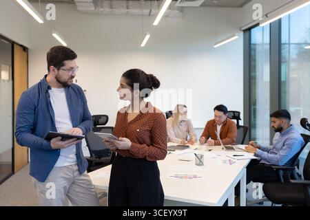 Office setting with diverse team members working together using laptops, tablets, and documents. Collaboration and synergy reflect a productive and dynamic professional environment Stock Photo