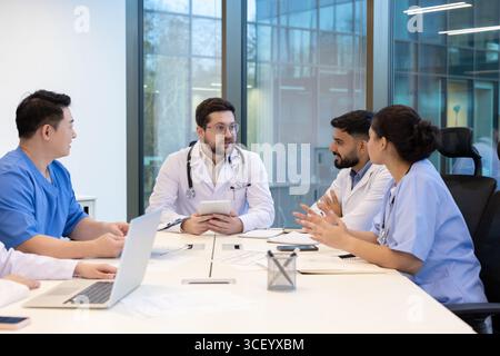 A diverse group of healthcare professionals collaborates during a team meeting in a modern clinic. The discussion focuses on improving patient care, teamwork, and professional collaboration Stock Photo