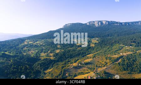 Sweeping mountain slopes and dramatic cliffs frame a quiet highland valley bathed in early morning light Stock Photo