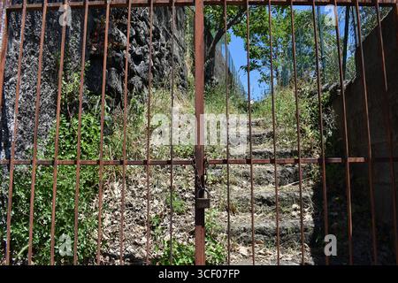 Property entrance gate with chain and lock. Entrance to a private vineyard and garden. Natural stone steps and walkway in a private garden. Stock Photo