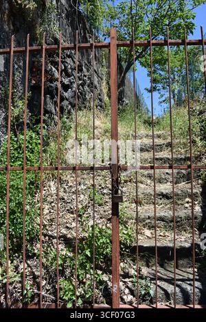 Property entrance gate with chain and lock. Entrance to a private vineyard and garden. Natural stone steps and walkway in a private garden. Stock Photo