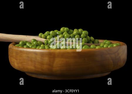 Wooden bowl with fresh peas and wooden spoon isolated on black background Stock Photo