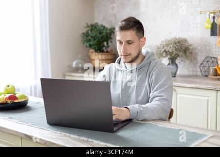 concentrated guy freelancer using computer, remote working in home office analyzing online data market  with laptop sit at kitchen Stock Photo