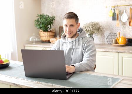 guy freelancer sit at kitchen desk with laptop. Bearded freelancer male remote working from home. man chat with friends online from home using pc. Stock Photo