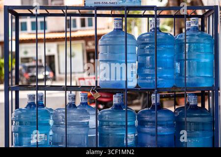 Big plastic water bottles stacked and secured in a metal cage outdoors, suggesting water delivery or storage for sale Stock Photo