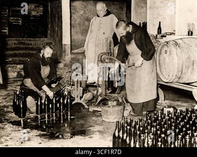 Three monks working at a Trappist brewery in Poperinghe, Belgium, 1927. Two monks are filling bottles while several bottles are seen on the ground. Stock Photo