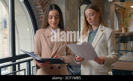 Business partners colleagues talking with papers documents Caucasian entrepreneurs workers women businesswomen girls female in corporate office Stock Photo